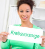 Bild: eine junge Frau hält lächelnd ein Schild "Krebsvorsorge"